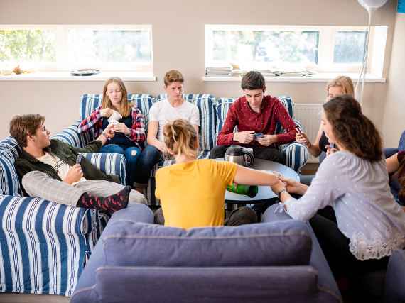 zu sehen sind Schülerinnen und Schüler die auf einer Couch rund um einen Tisch sitzen und Karten spielen