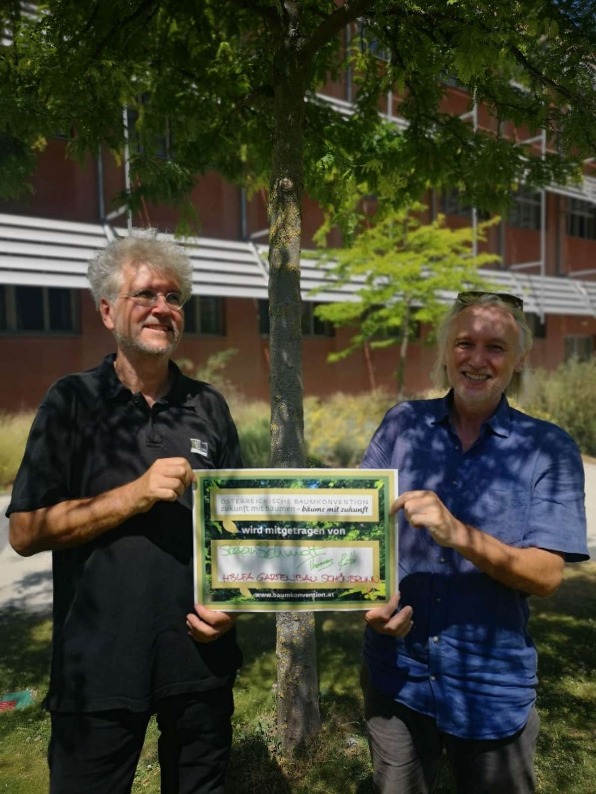 Stefan Schmidt und Thomas Roth stehen mit der unterzeichneten Baumkonvention vor einem Baum im Schulgarten