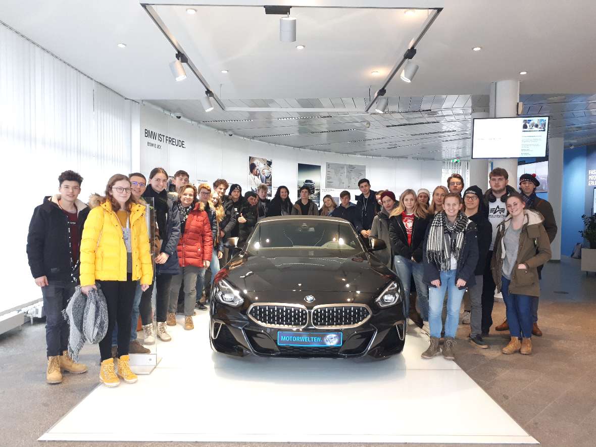 zu sehen sind Schülerinnen und Schüler in einer Fabrikshalle, die rund um ein Auto stehen 