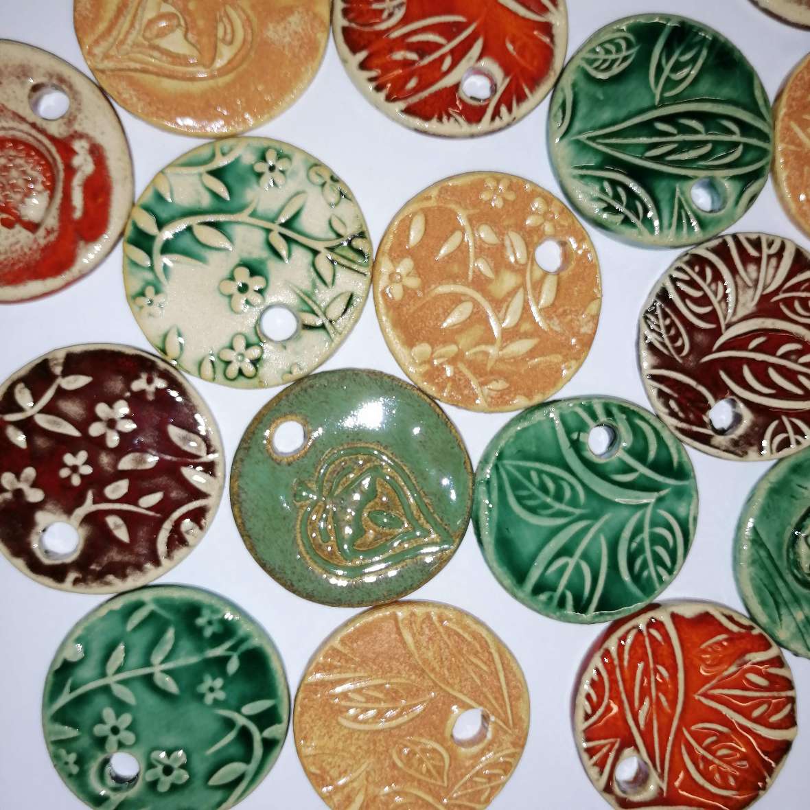 zu sehen sind fertig gebrannte Blumen-Medaillons mit floralem Aufdruck in den Farben rot, grün, orange und gelb
