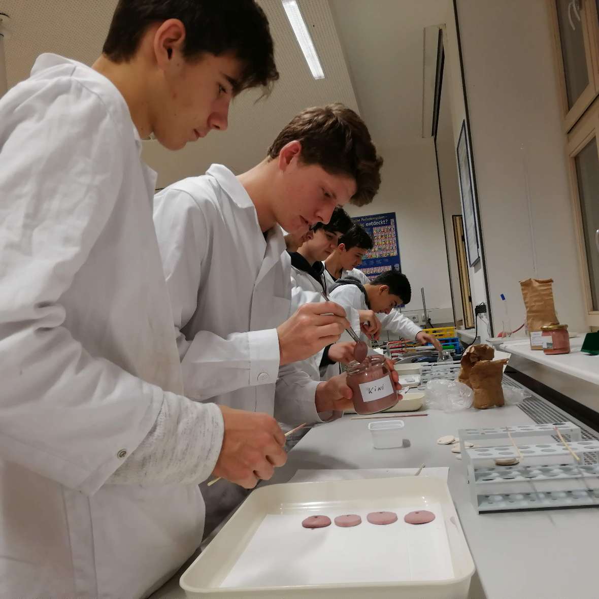 zu sehen sind Schüler, die die rohen Ton-Medaillons in eine rote Farbe tauchen