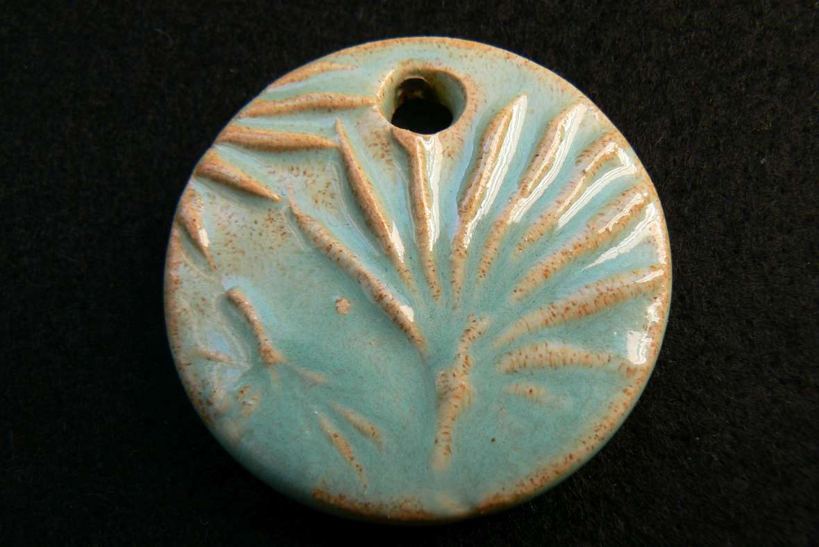 zu sehen ist ein fertig gebranntes Medaillon mit einem Blumenabdruck in türkiser Farbe