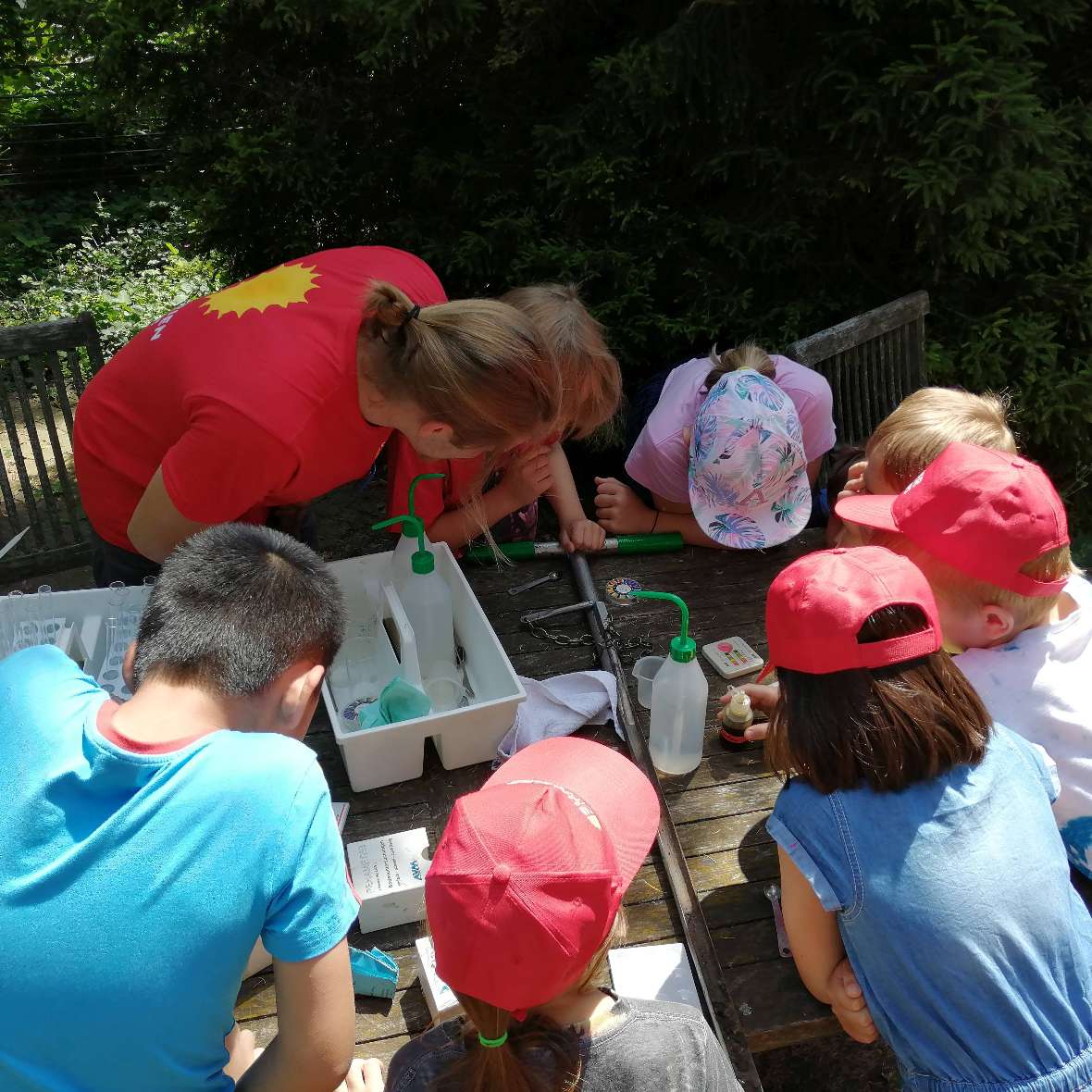 Sieben Kinder und ein Betreuer beugen sich über einen Holztisch und beobachten Bodenproben