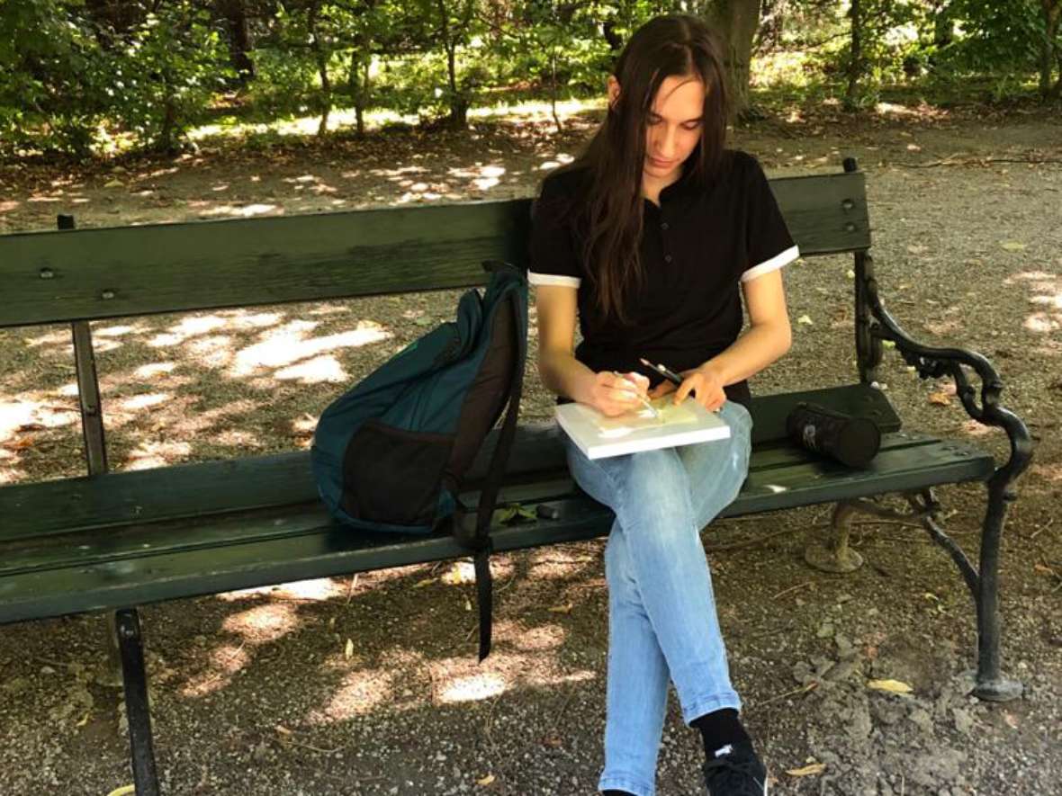 Ein Schüler skizziert auf einer Parkbank sitzend
