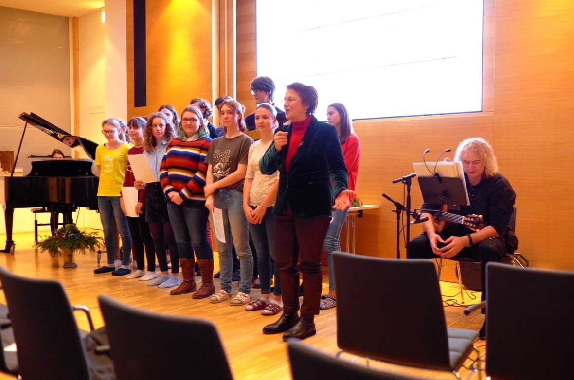 zu sehen sind Mädchen und Burschen die in einer Reihe stehen, daneben sitzt ein Mann mit einer Gitarre