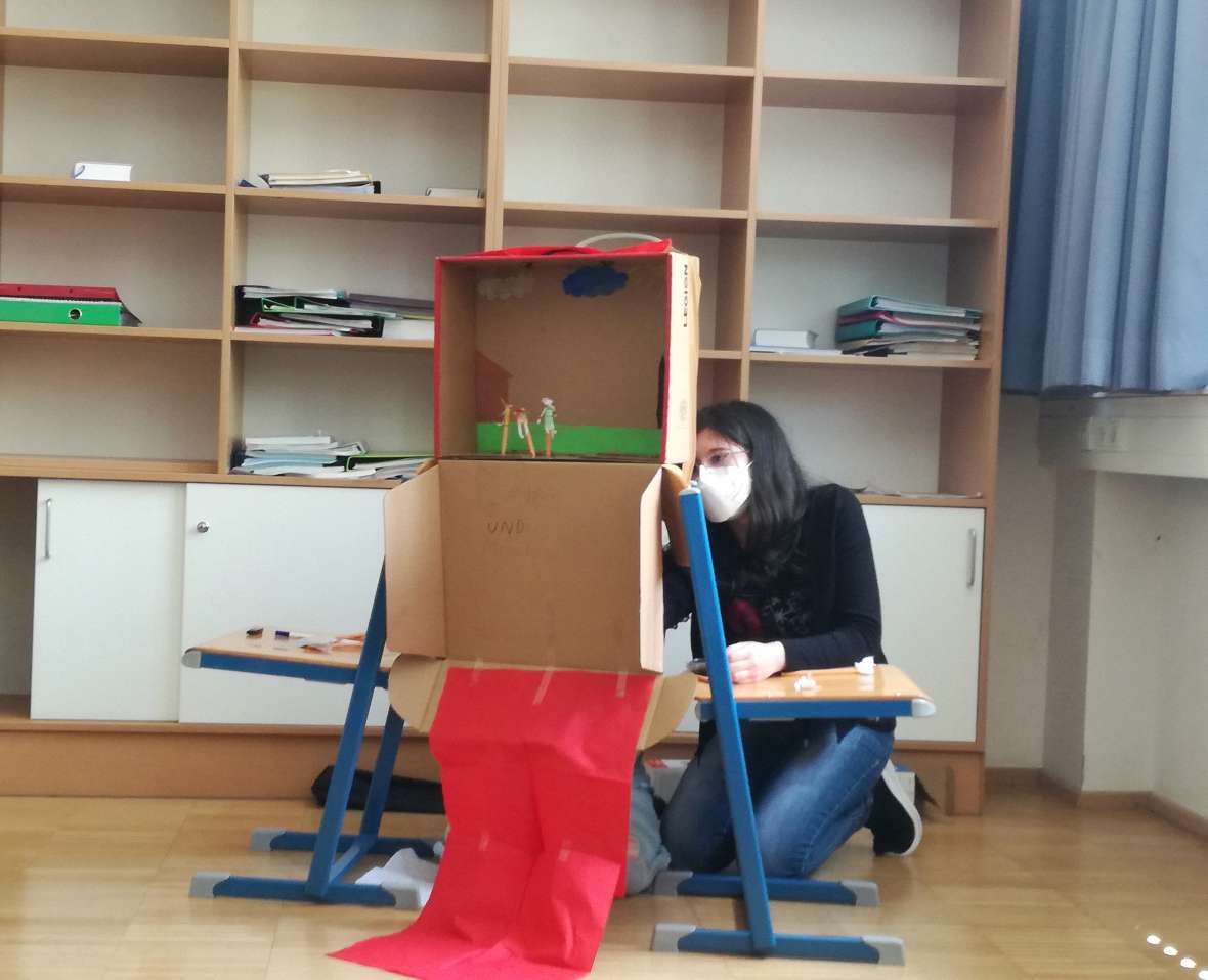 Eine Schülerin hockt hinter einem aus Pappe selbst gebastelten Puppentheater