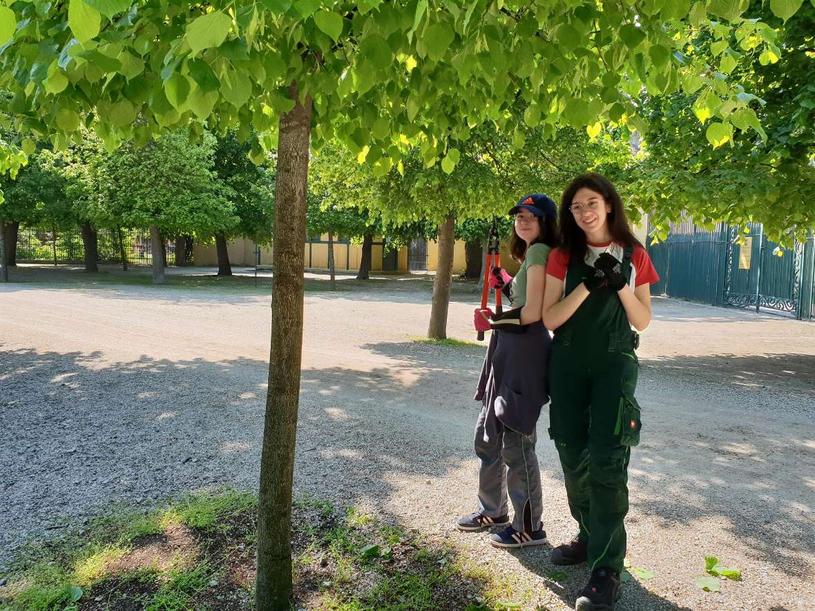 Zwei Schülerinnen posieren mit einer Heckenschere ausgestattet im Schlosspark