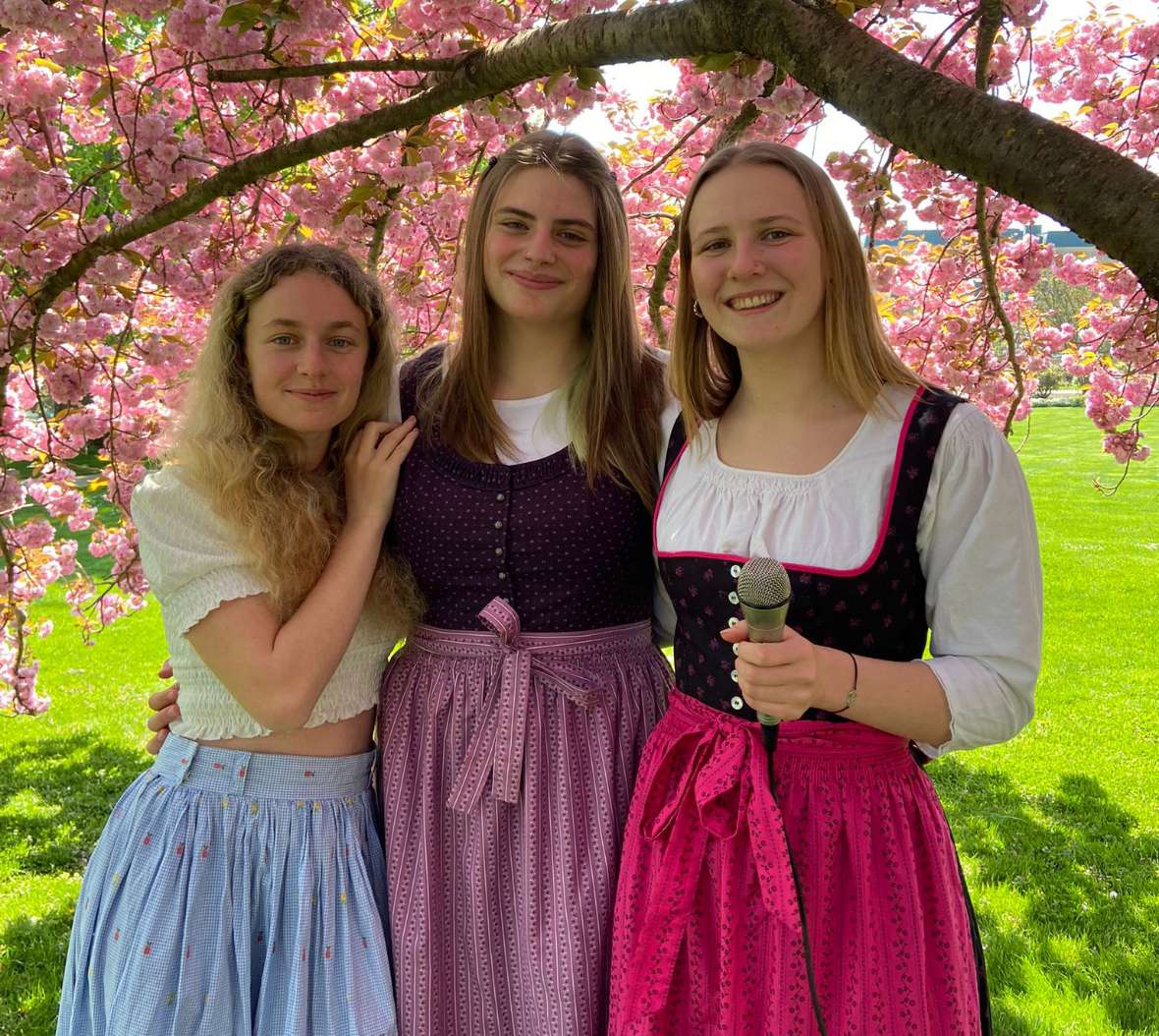 Drei Schülerinnen im Dirndl stehen unter einem blühenden Kirschbaum