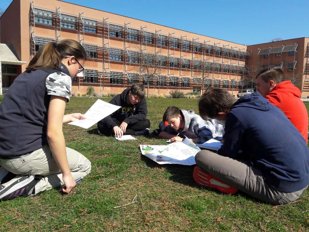 Schüler:innen auf der großen Wiese vor dem Schulgebäude mit Arbeitsblättern zum Thema Kunststoffe und Alternativen
