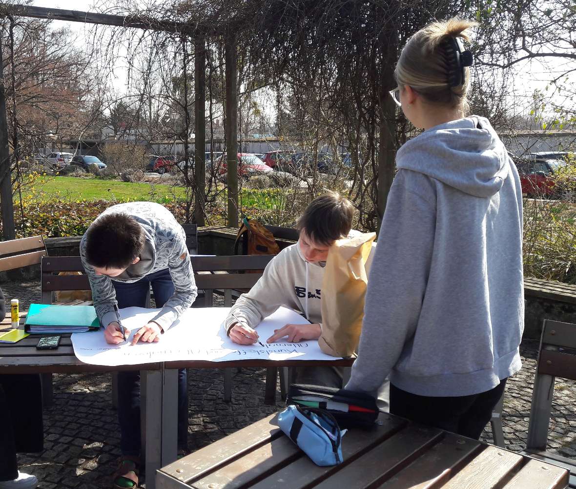 Schüler:innen beim Erstellen eines Posters im Schulgarten