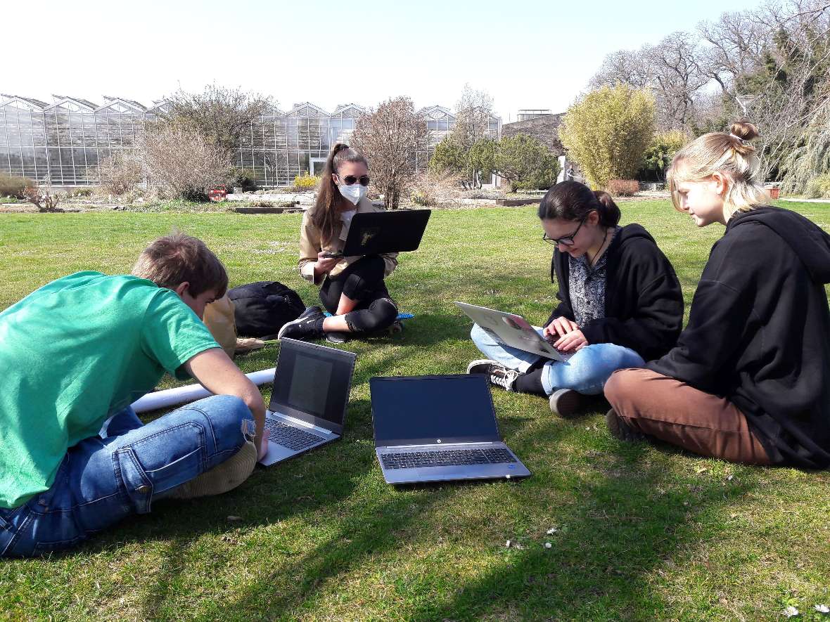 Schüler:innen arbeiten auf ihren Laptops im Schulgarten