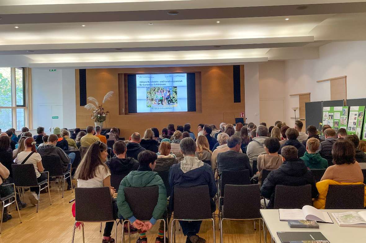 Personen sitzen im Festsaal und sehen sich eine Schulpräsentation an