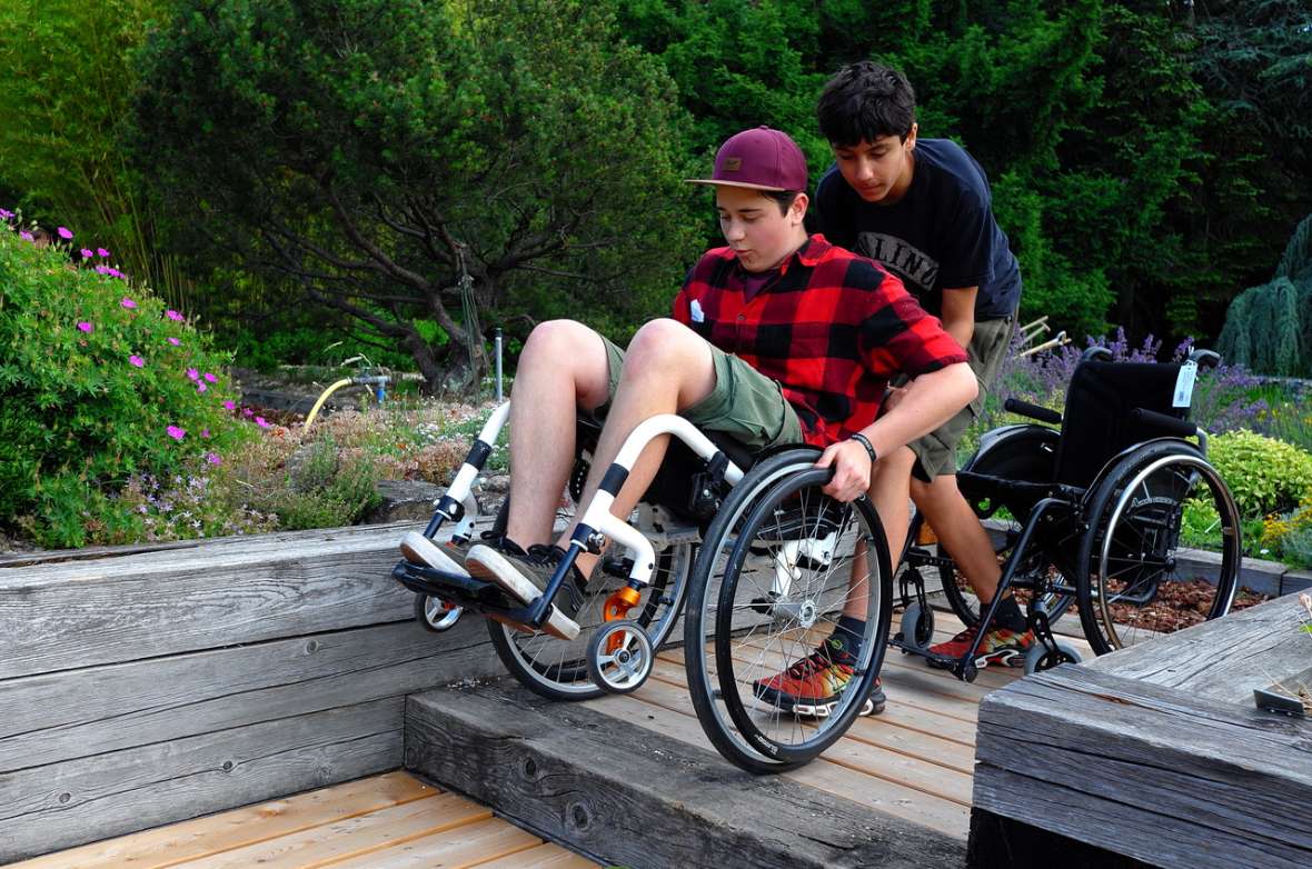 Schüler im Rollstuhl wird von einem Schüler über Treppen im Schulgarten gefahren