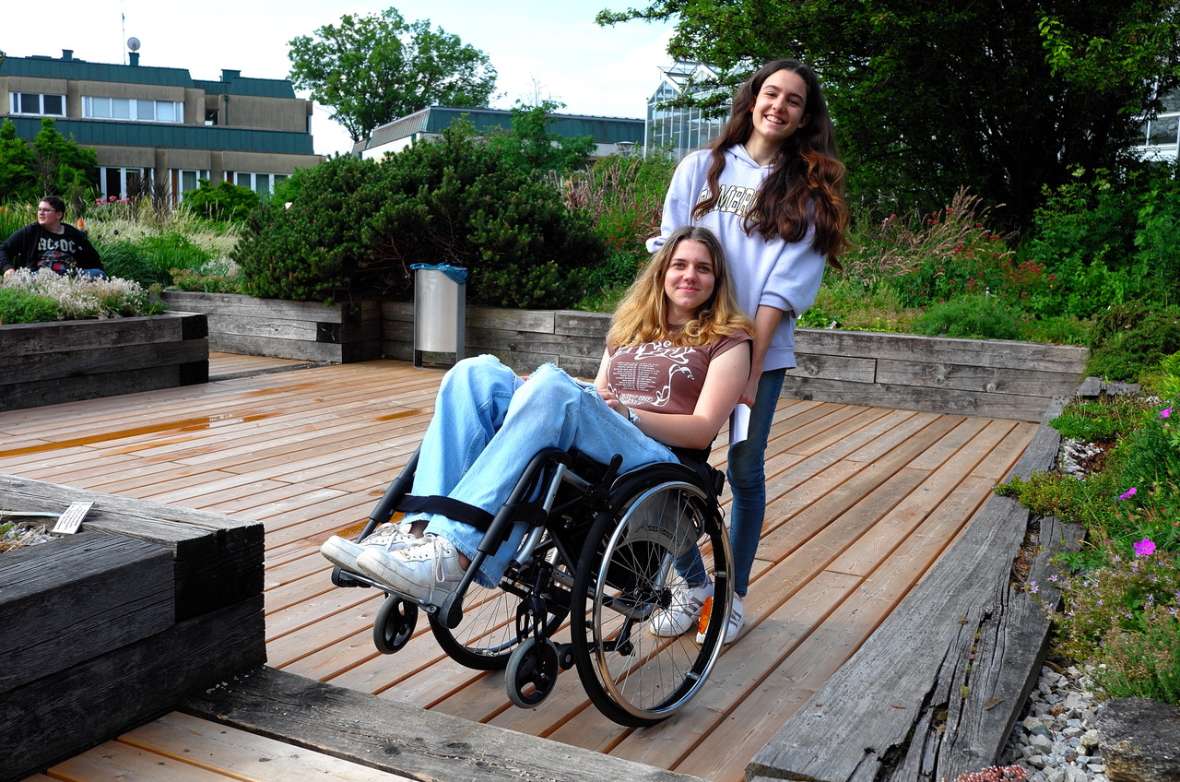 Schülerin hilft einer Mitschülerin im Rollstuhl beim Überwinden einer Treppe im Schulgarten