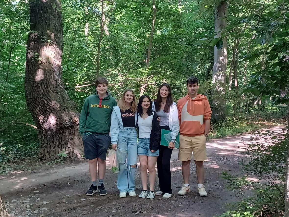 Drei Schülerinnen und zwei Schüler stehen in einer Waldkulisse