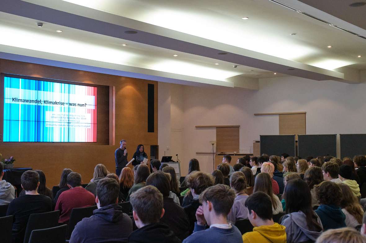 Schülerinnen und Schüler sitzen im Festsaal und blicken auf die Videoleinwand