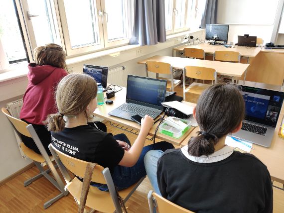 Drei Schülerinnen sitzen vor Laptops und nehmen an einer Online-Besprechung teil