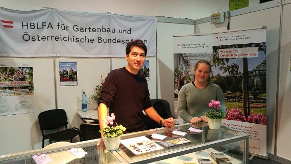 Eine Schülerin und ein Lehrer posieren vor dem Messestand der Schule